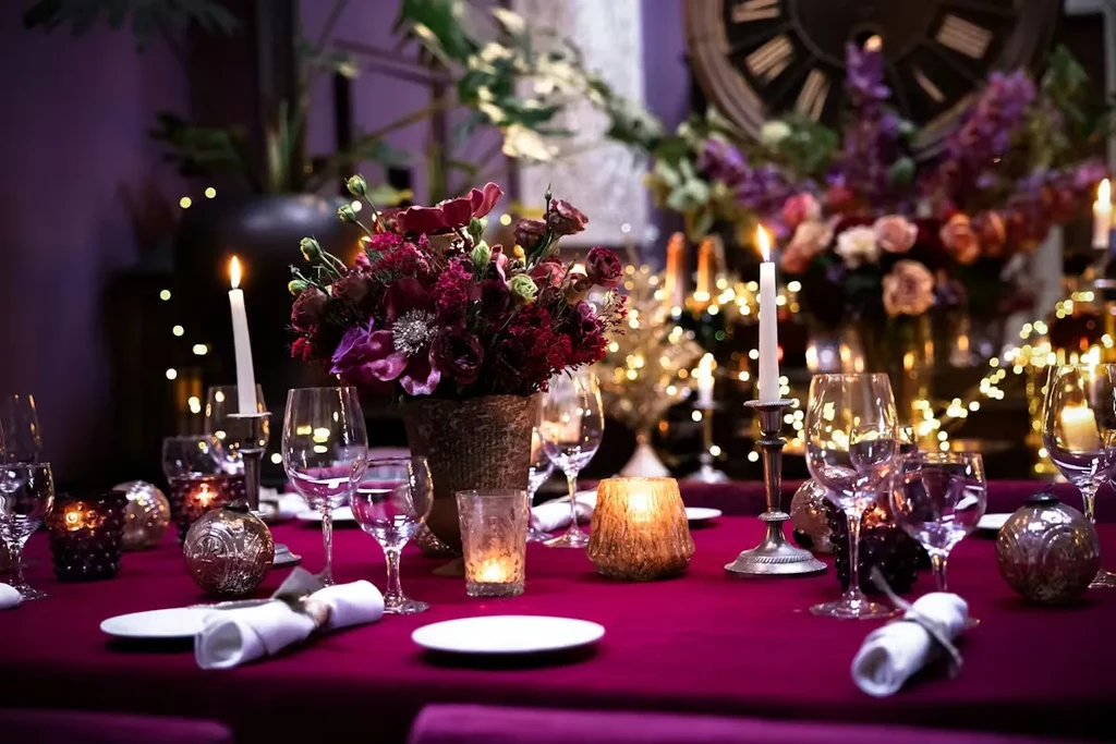 Dimly lit dining table with dark flowers, candles, and string lights.