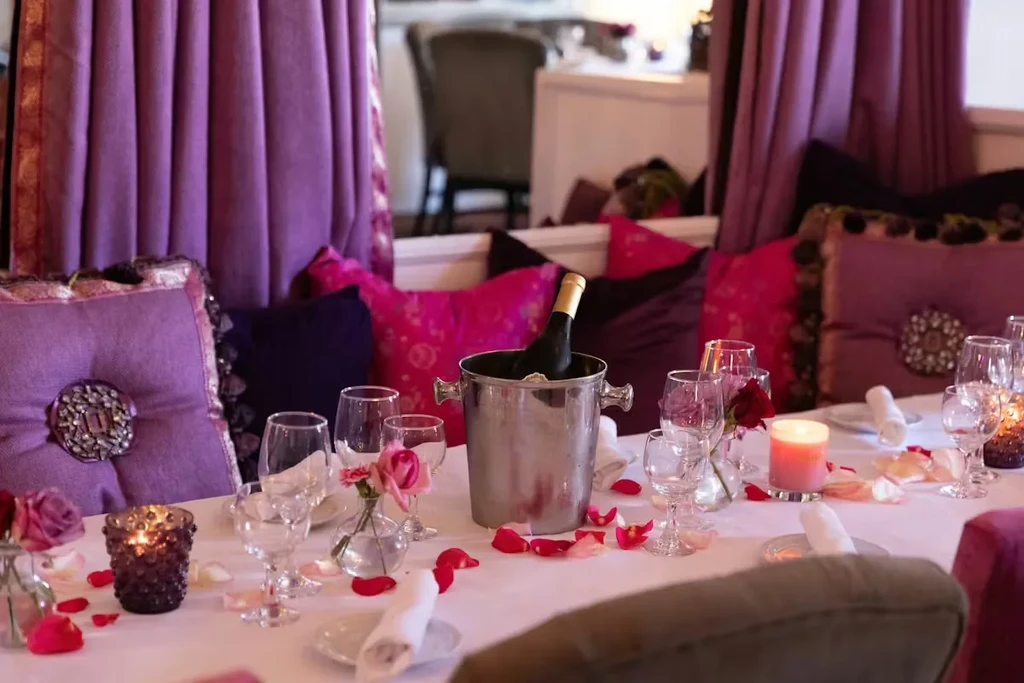 Elegant restaurant table set with wine, roses, and lit candles.
