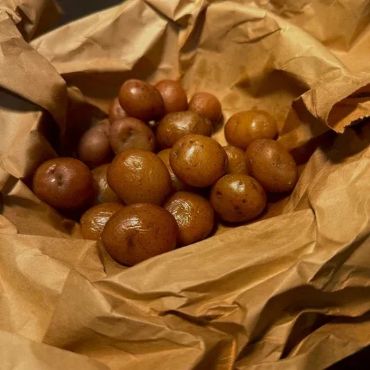 Several roasted golden-brown potatoes in a crumpled brown paper bag.