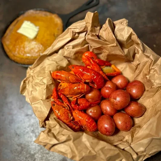 Cooked crawfish and potatoes on paper; cornbread with melting butter.