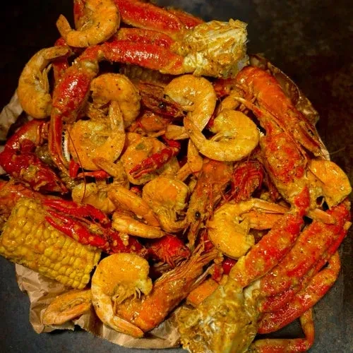 Glossy, seasoned crab legs, shrimp, crawfish, and corn on paper.