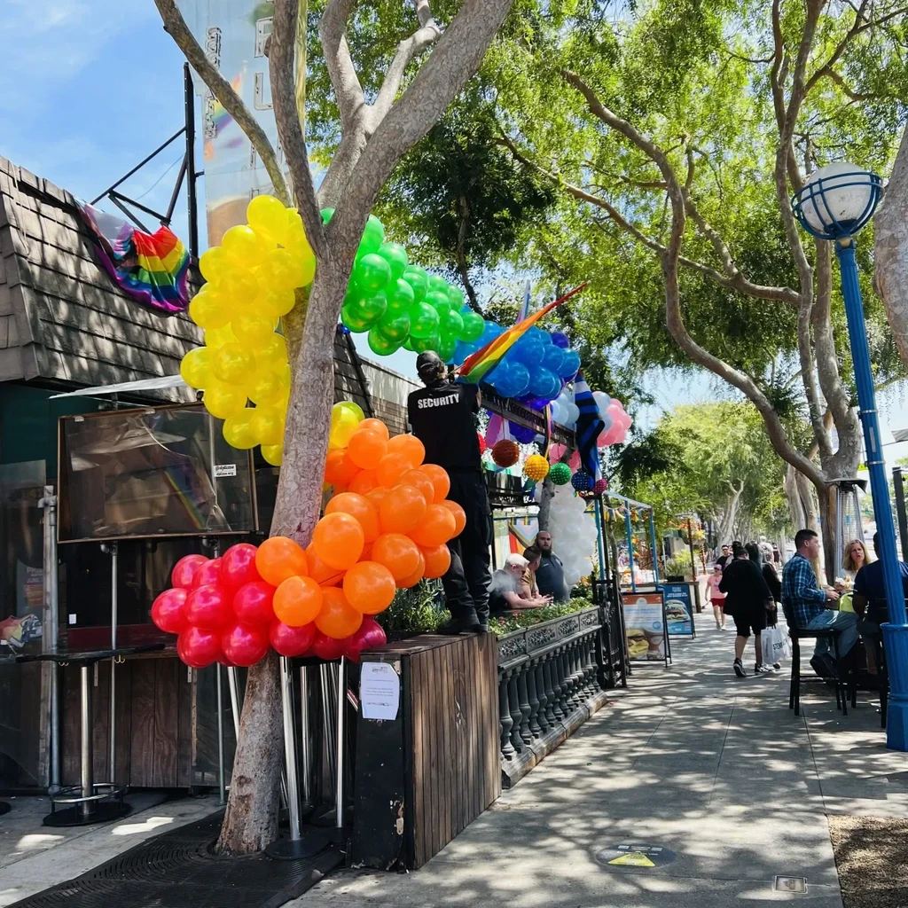 Tree with rainbow balloons, security staff, and outdoor diners.