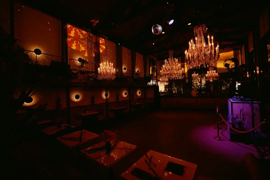 Dimly lit, opulent venue with crystal chandeliers, fiery screen, and DJ booth.