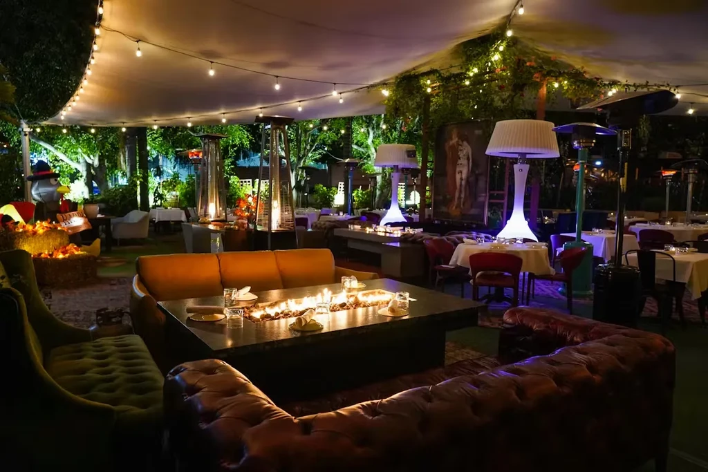 Nighttime outdoor restaurant lounge, fire pit, string lights, and diverse seating.