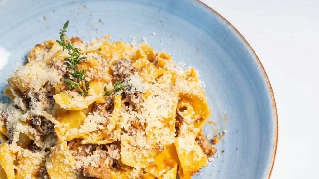 Close-up of pappardelle pasta with ragu, grated cheese, and thyme.