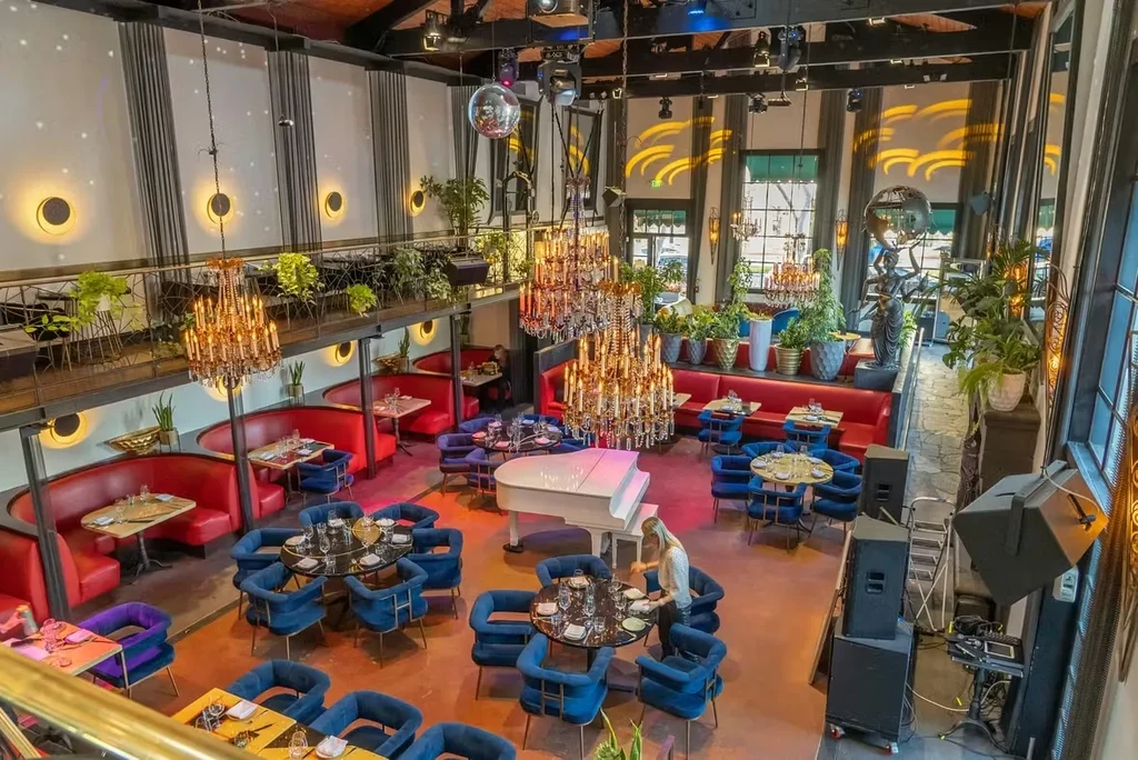 Opulent two-story restaurant interior with grand piano, booths, and blue chairs.