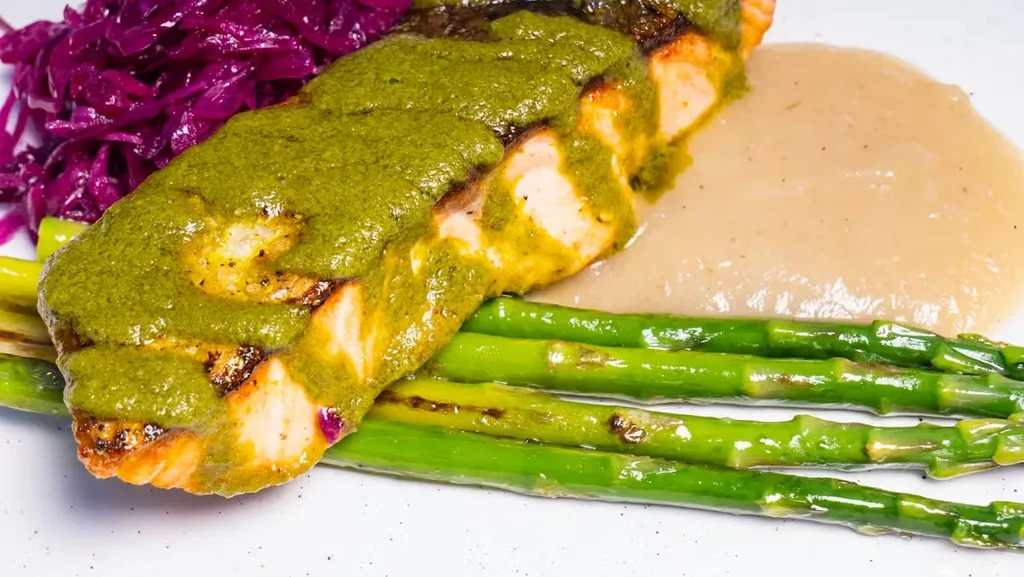 Professionally plated salmon with green sauce, asparagus, purple cabbage, and puree.