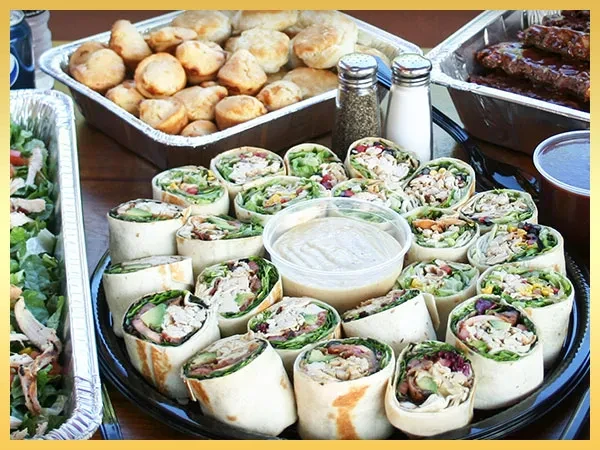 Catered buffet: platter of wraps, chicken salad, biscuits, and BBQ ribs.
