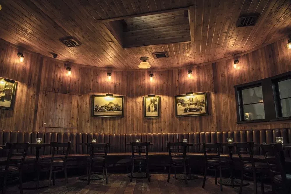 Curved restaurant interior with wood paneling, leather banquette, warm lighting.