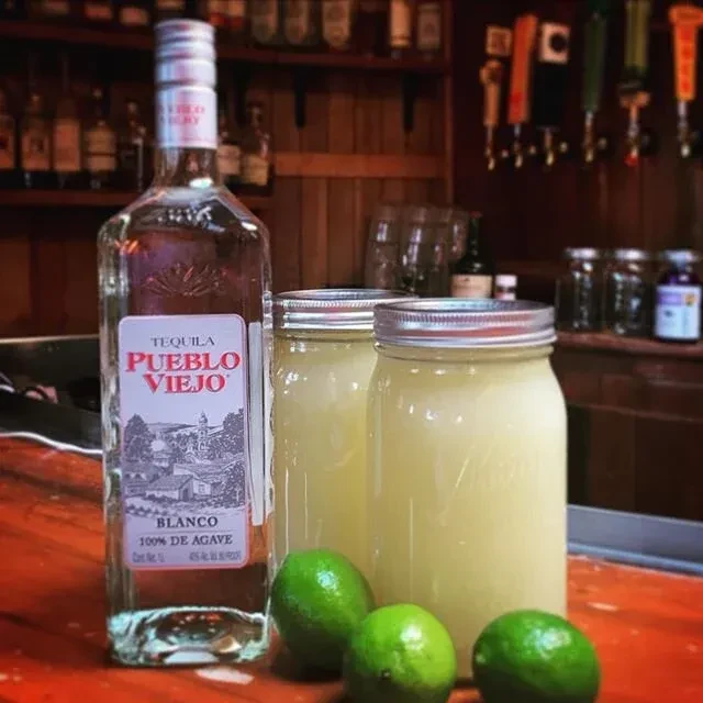 Pueblo Viejo Tequila Blanco, jars, and limes on a rustic bar.