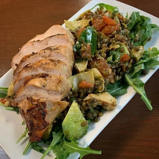Plated grilled chicken, lentil and vegetable salad, with arugula.