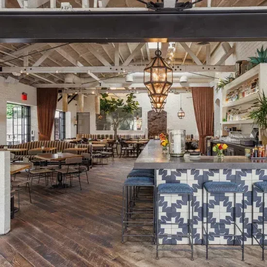 Restaurant interior with tiled bar, banquettes, high ceiling, and warm lantern lighting.