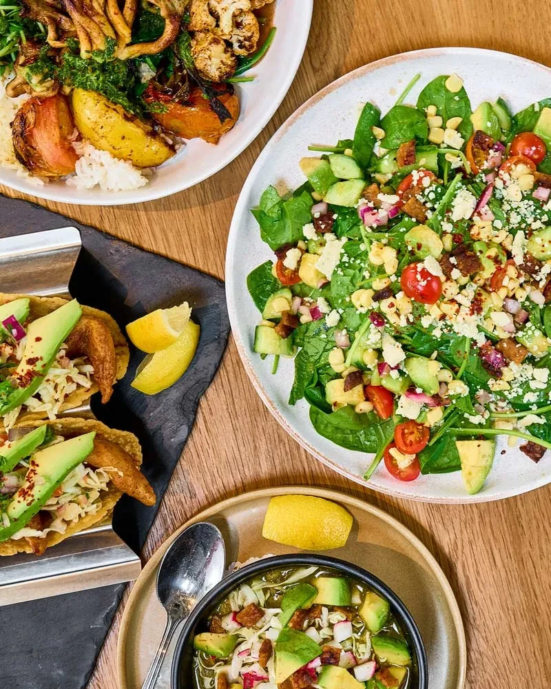 Top-down view of colorful rice, salad, soup, and tacos on wood.