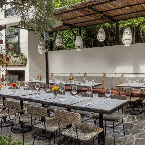 Rustic restaurant patio with set tables, shaded canopy, and banquette seating.