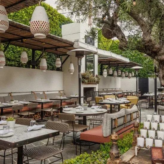 Chic outdoor restaurant patio with tree, lanterns, and set tables.