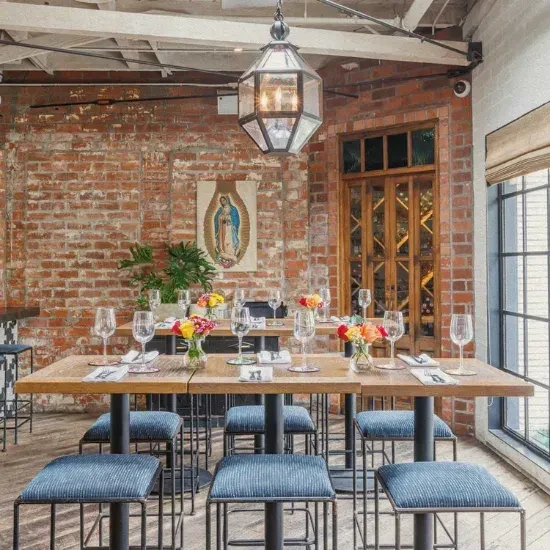 Restaurant interior: communal tables, blue stools, brick wall, ornate chandelier.