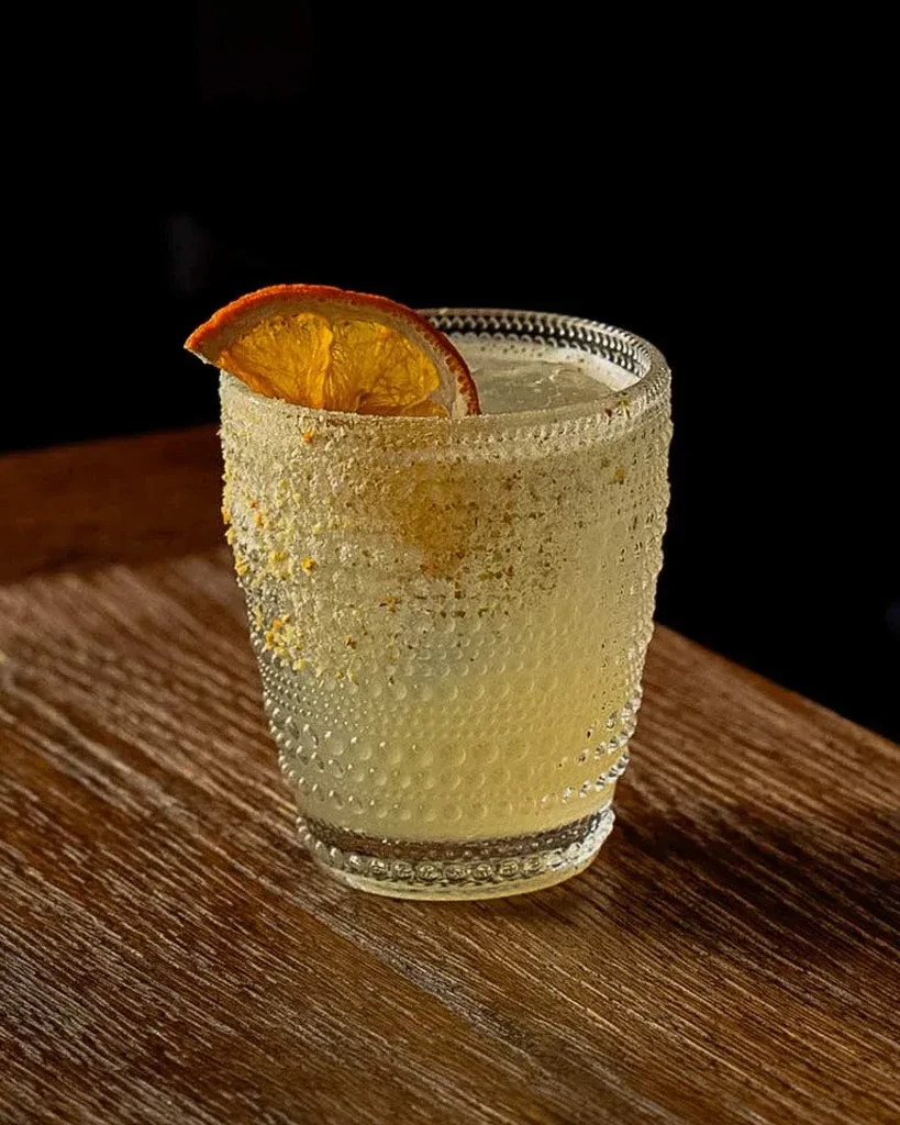Textured glass cocktail with sugared rim and dried orange on rustic wood.