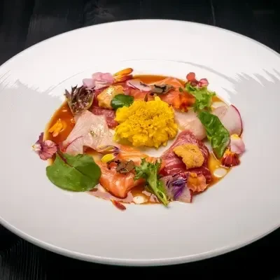 Artfully arranged sashimi with gold leaf, yellow purée, and edible flowers.