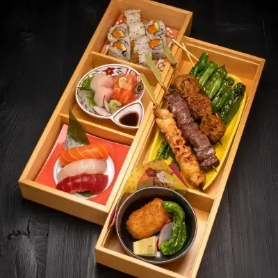 A multi-compartment Japanese meal with sushi, sashimi, yakitori, and katsu.