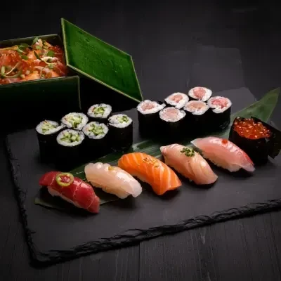 Assorted Japanese sushi, sashimi, and ikura rice bowl on dark slate.