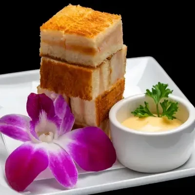Crispy golden food stack, sauce, and purple orchid on white plate.