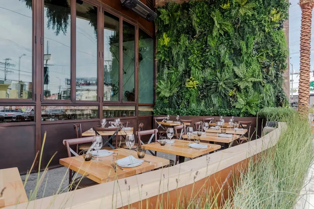 Modern restaurant patio with a vibrant green living wall and set tables.