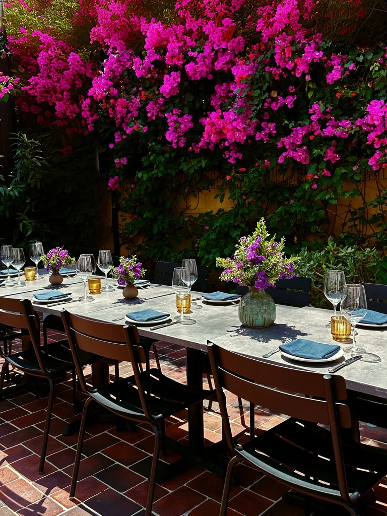 Outdoor dining table with place settings under fuchsia bougainvillea.