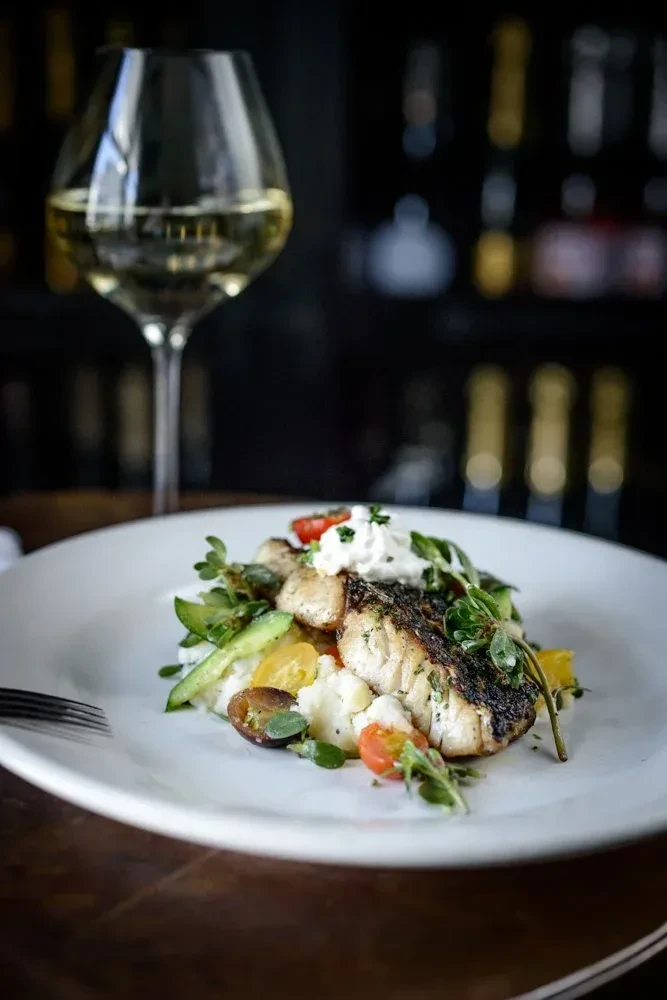 Grilled fish, white sauce, colorful vegetables, purée, and wine glass.