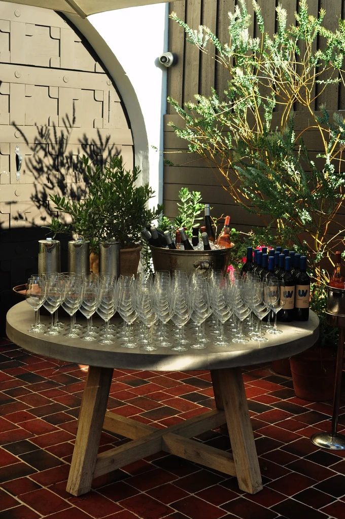 Outdoor table with numerous wine glasses, bottles, and plants.