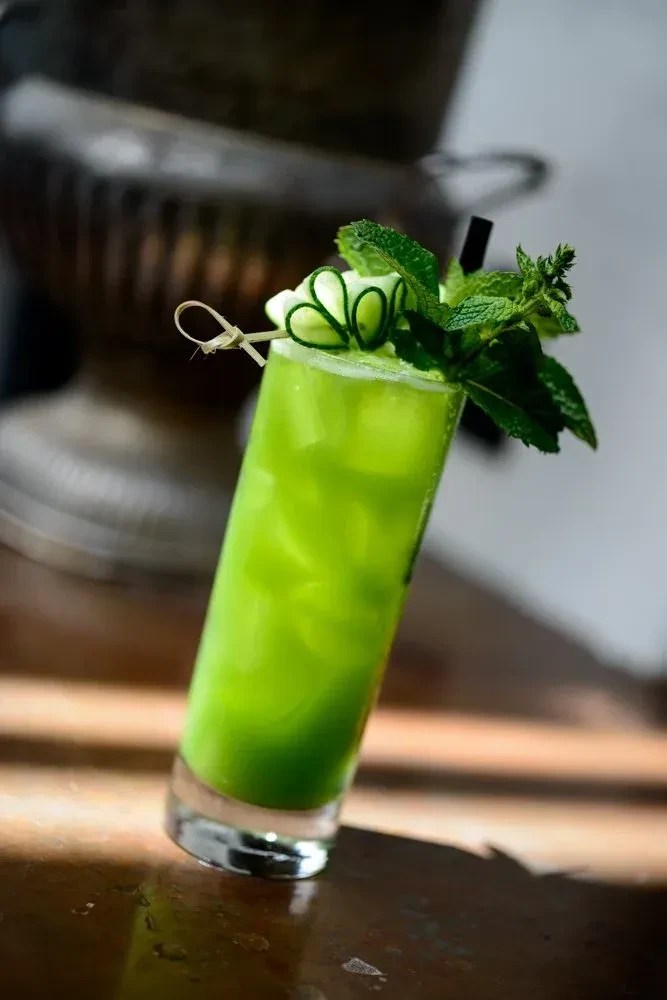 Layered green cocktail with mint and cucumber on dark wood.