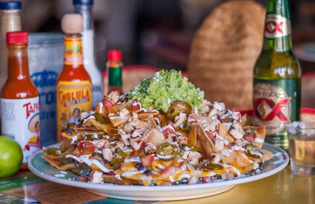 Piled high nachos with cheese, chicken, guacamole, jalapeños, and hot sauces.
