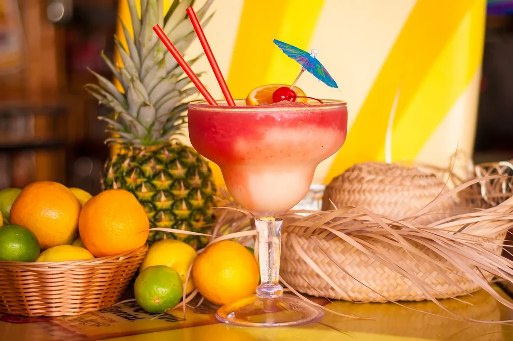 Layered frozen drink in margarita glass with tropical fruit and decor.
