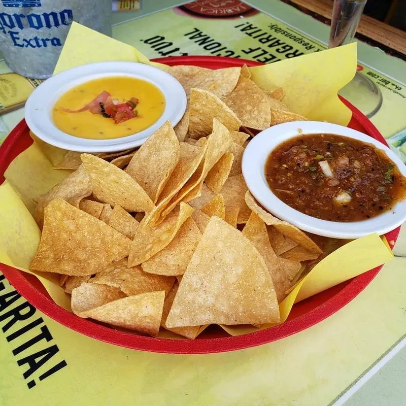 Tortilla chips with queso and salsa dips in a red basket.