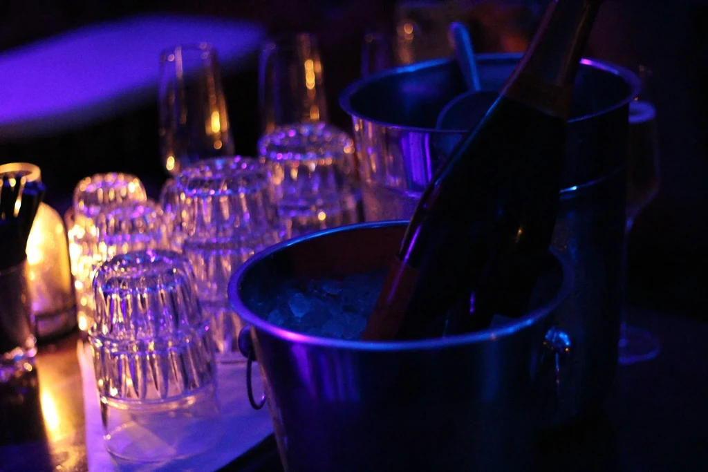 Purple-lit bar with champagne, ice bucket, and stacked drinking glasses.