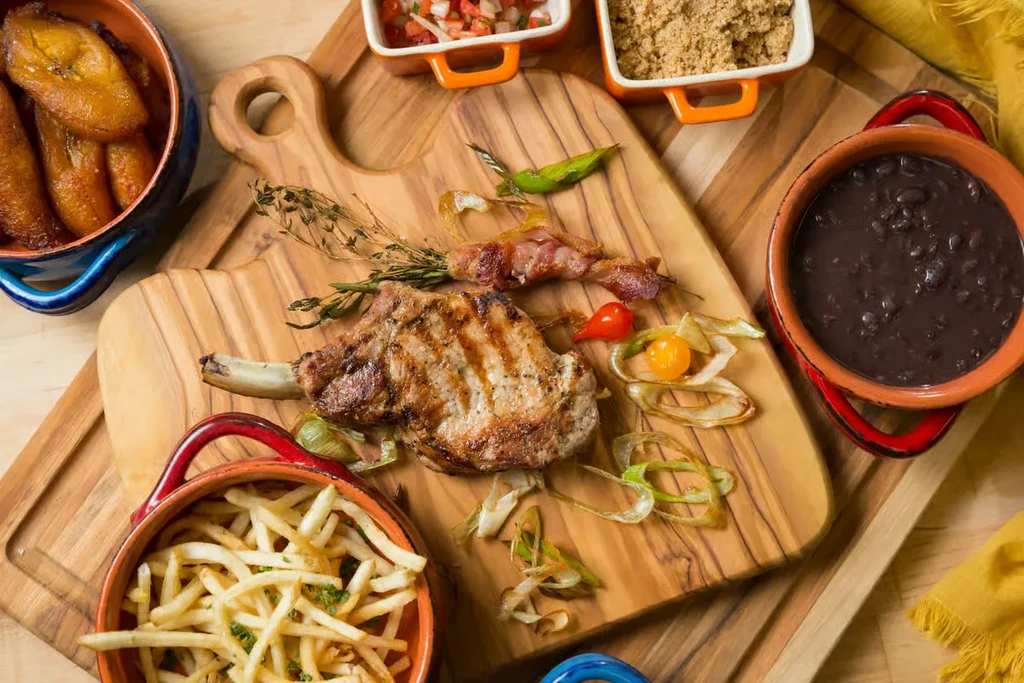 Grilled pork chop, fries, beans, plantains, and salsa on rustic wooden boards.