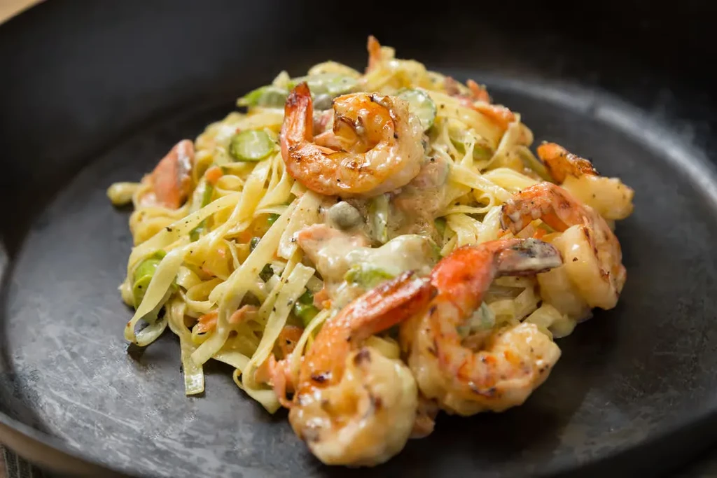 Creamy pasta with grilled shrimp and green vegetables in a dark pan.