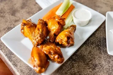 Plate of buffalo chicken wings, celery, carrots, and dipping sauce.