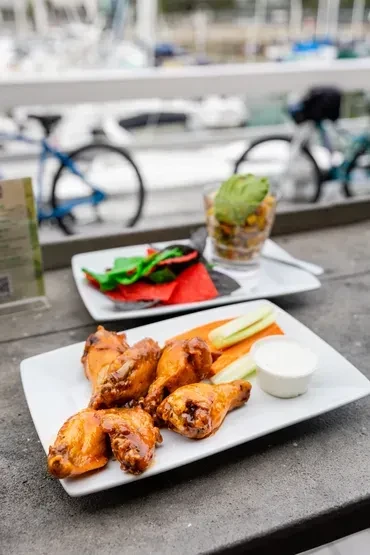 Chicken wings, colorful food, and a layered drink on a dark table.