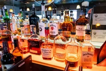 Neatly arranged whiskey and bourbon bottles on a lighted bar.