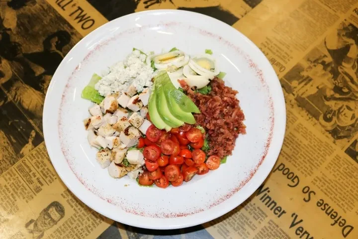 Overhead view of a vibrant Cobb salad on a vintage newspaper background.