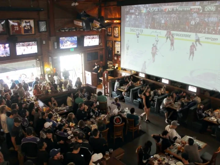 Bustling sports bar with huge screen showing hockey game, many patrons.