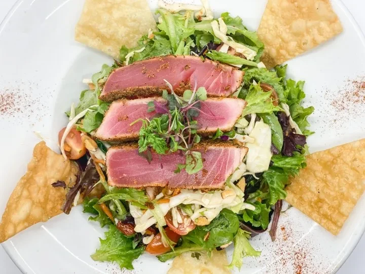 Seared medium-rare tuna slices on mixed greens with crispy chips.