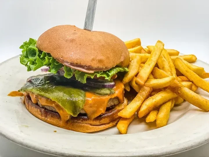 Gourmet burger with green pepper, red onion, lettuce, and golden fries.