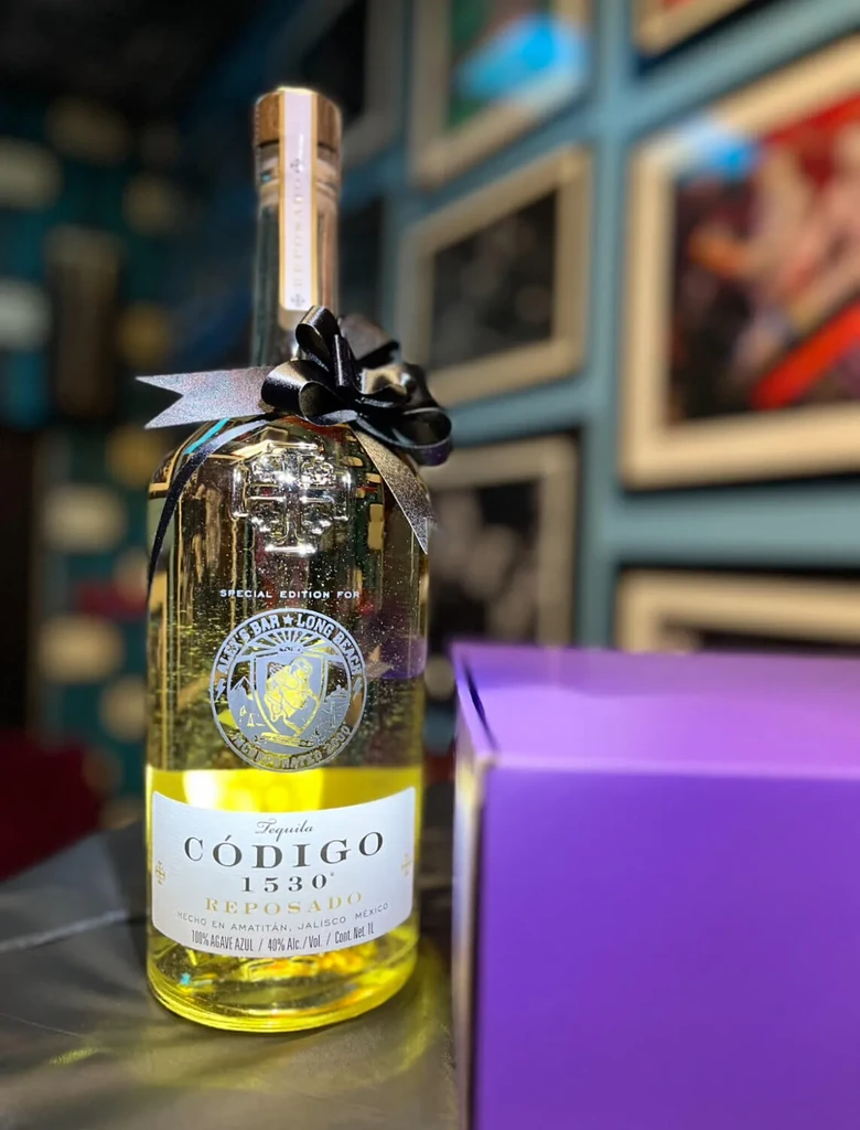 Ornate golden Código 1530 Reposado tequila bottle, blurred gallery background.