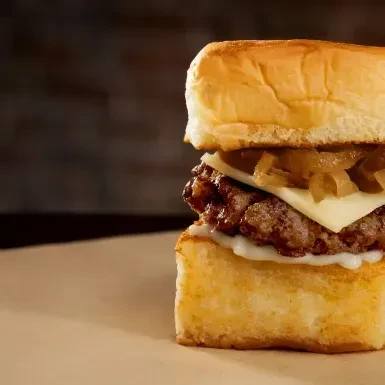 Close-up: Slider burger with golden bun, patty, melted cheese, caramelized onions.