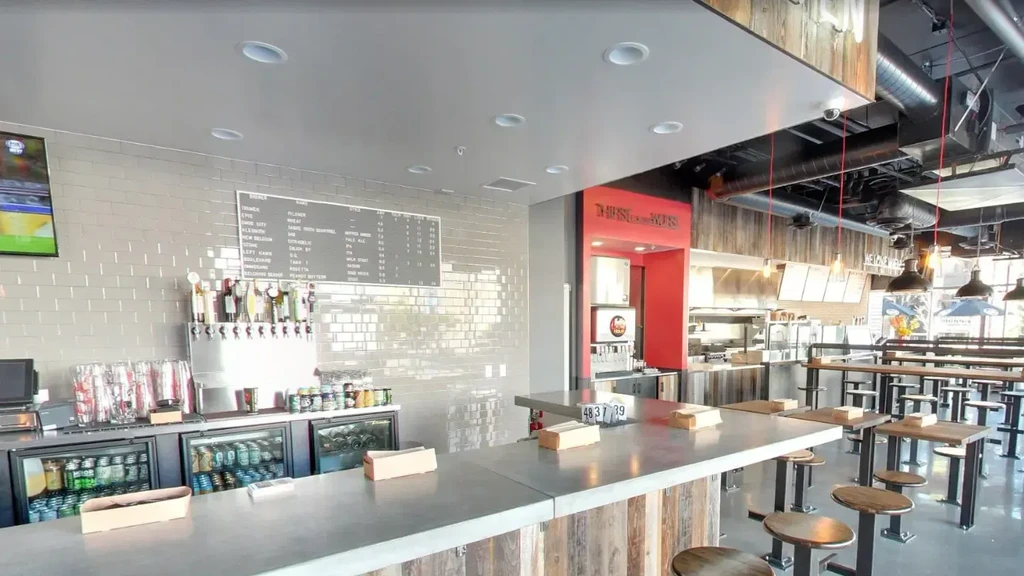 Empty modern industrial bar with beer taps, menu, and open kitchen.