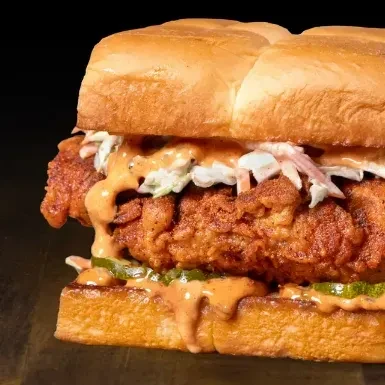 Close-up: Crispy fried chicken sandwich with coleslaw, pickles, and sauce.