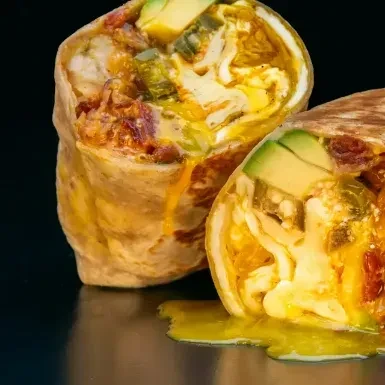 Breakfast burrito halves reveal eggs, avocado, peppers, and meat.