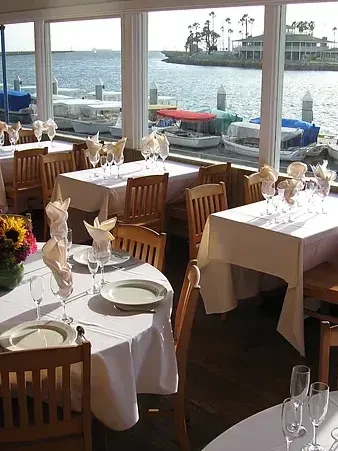 Empty, sunlit waterfront restaurant with set tables and a harbor view.