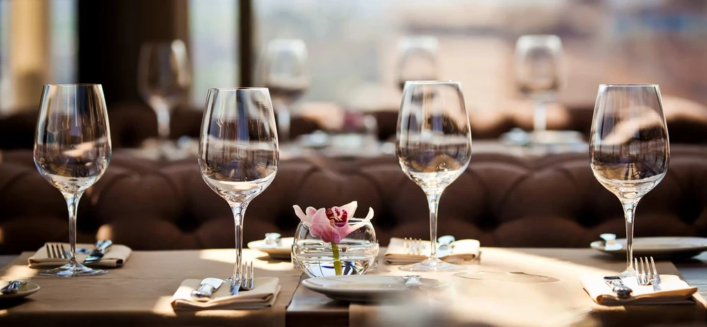 Restaurant table set with five empty wine glasses and pink orchid.